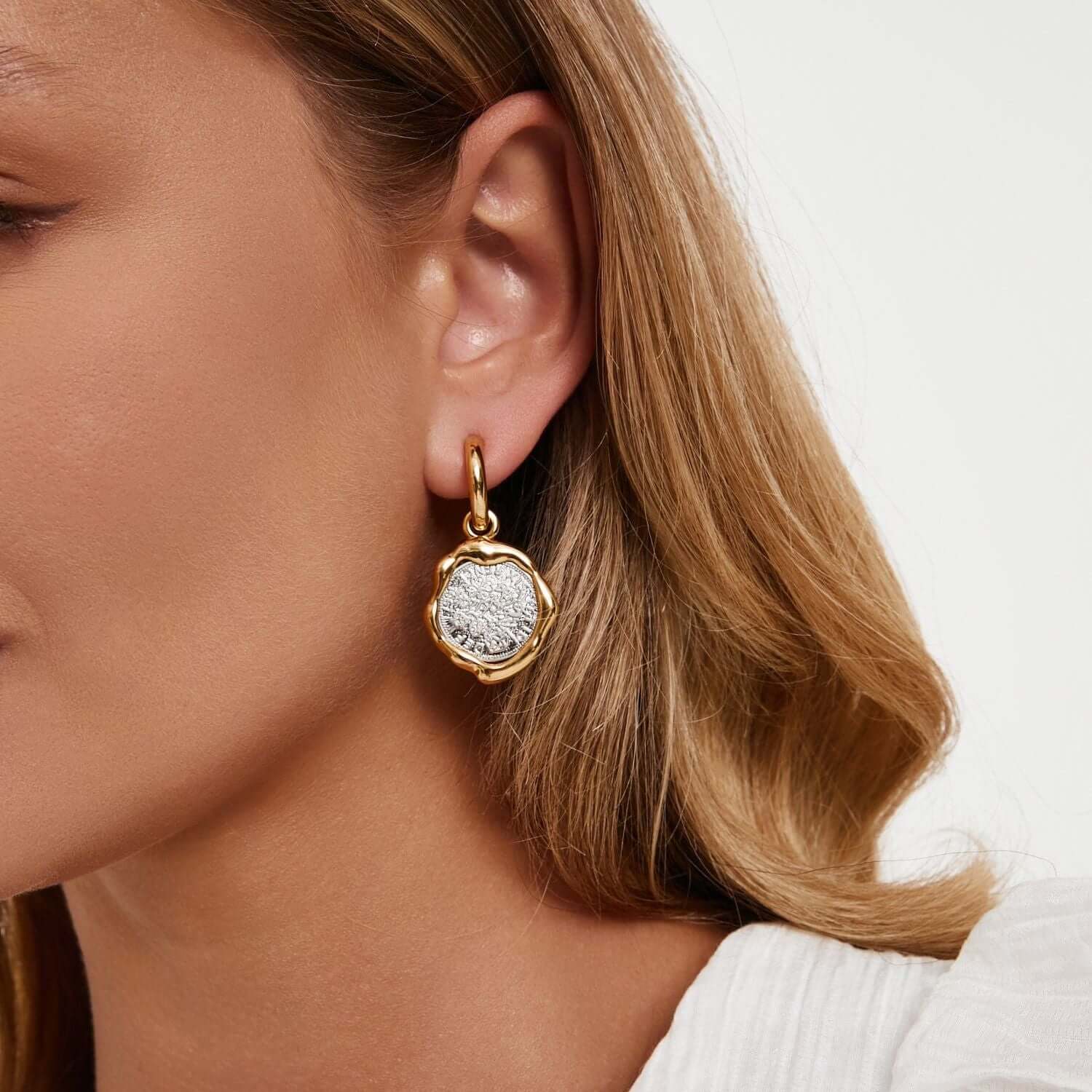 Woman wearing Earrings Coiné, gold-plated brass earrings with textured antique coin design, showcasing timeless beauty.