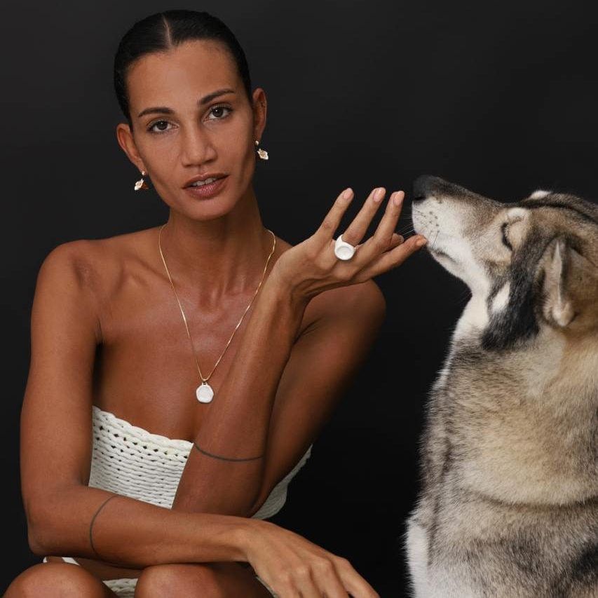 Woman showcasing Ring Alba while posing with a dog against a black background, highlighting elegance and simplicity.