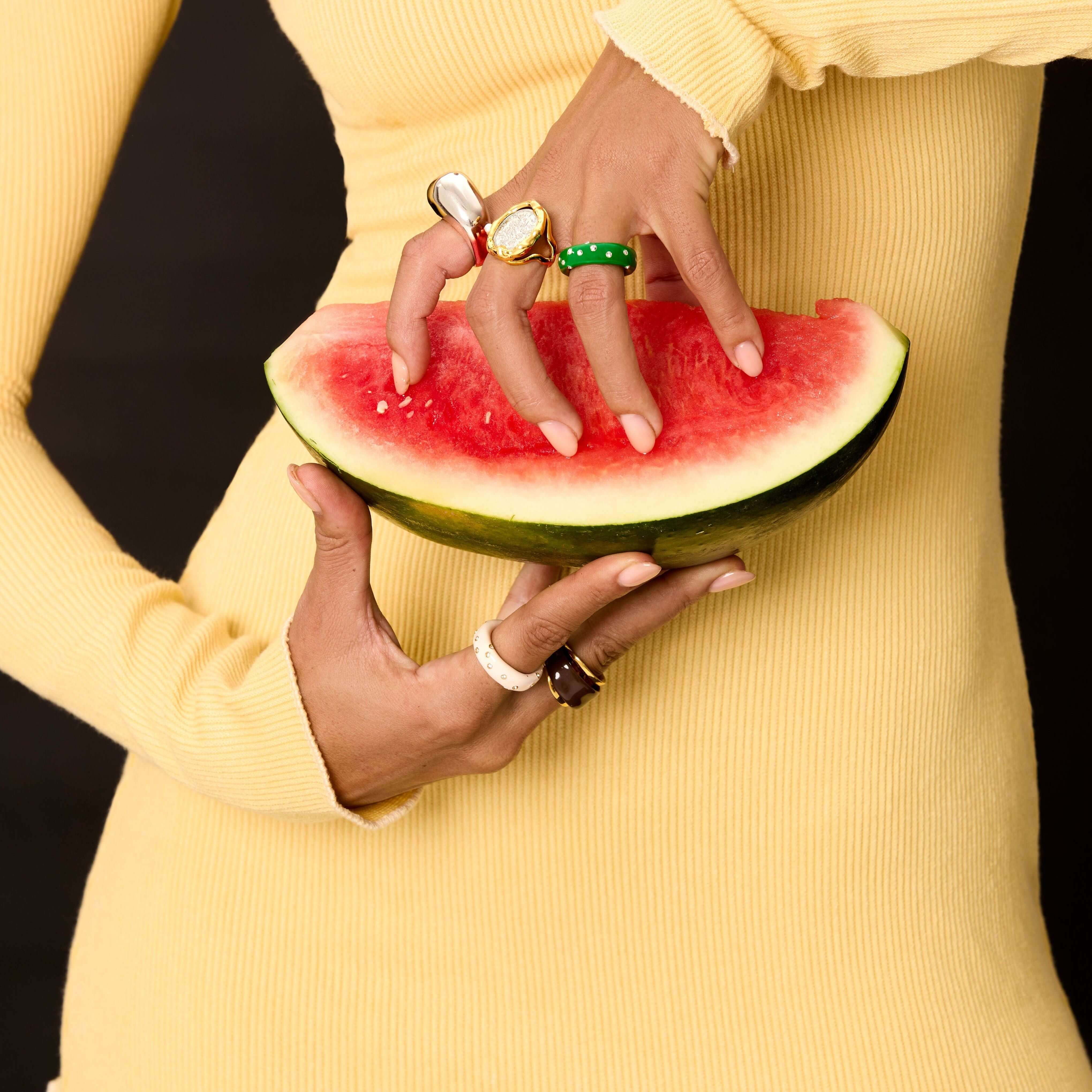 A model wearing multiple colorful rings, including the Ring Verdé, while holding a slice of watermelon.