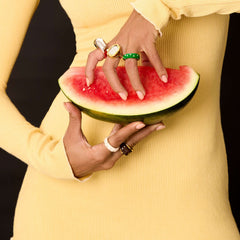 A model wearing multiple colorful rings, including the Ring Verdé, while holding a slice of watermelon.