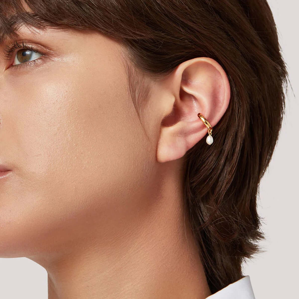 Earcuff Drop featuring a brass, gold-plated design with a suspended freshwater pearl on the upper ear.