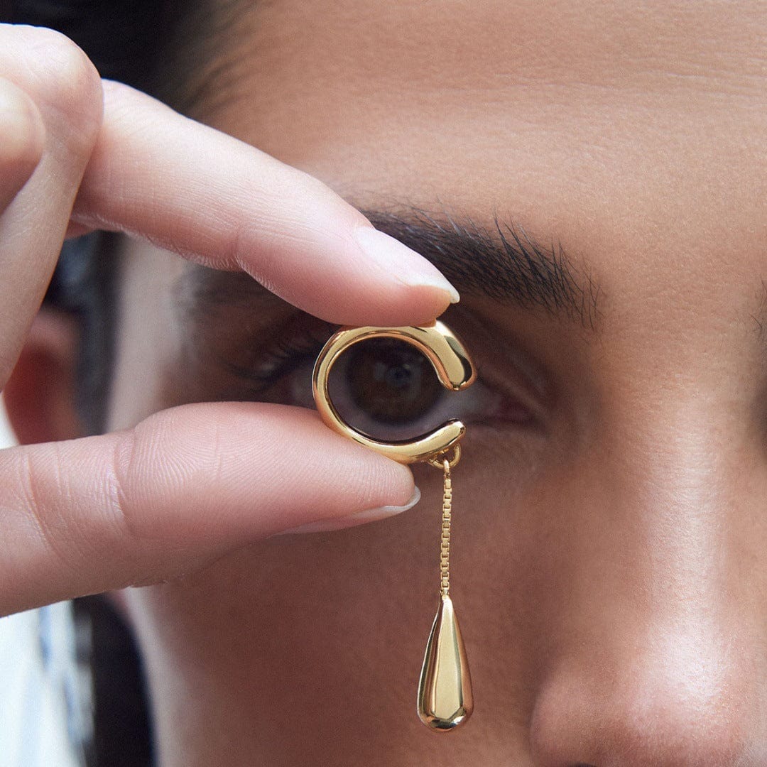 Earcuff Dew elegantly showcased, a gold-plated brass earring resembling a dew drop, held by a model.
