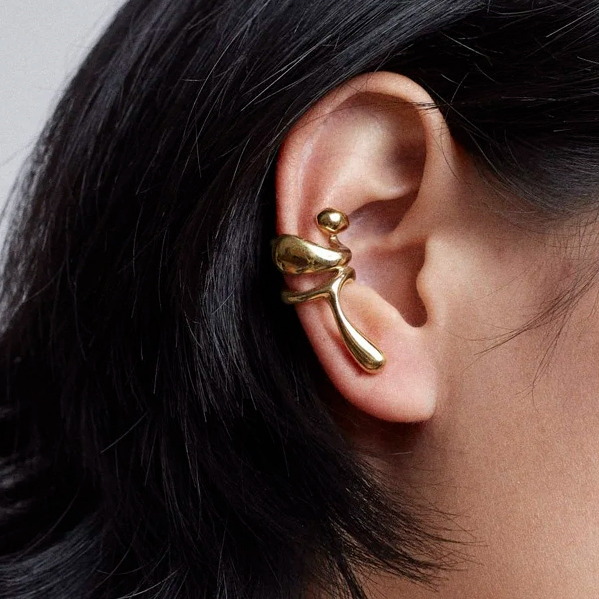 Close-up of Earcuff Lilt, a gold-plated brass accessory, showcasing its elegant curves on a model's ear.