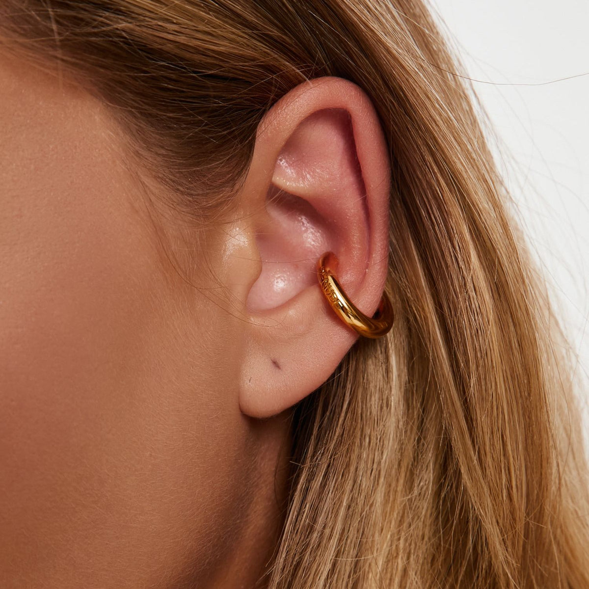 Earcuff Renude - polished gold cuff earring on ear, showcasing sleek design and minimalist elegance.