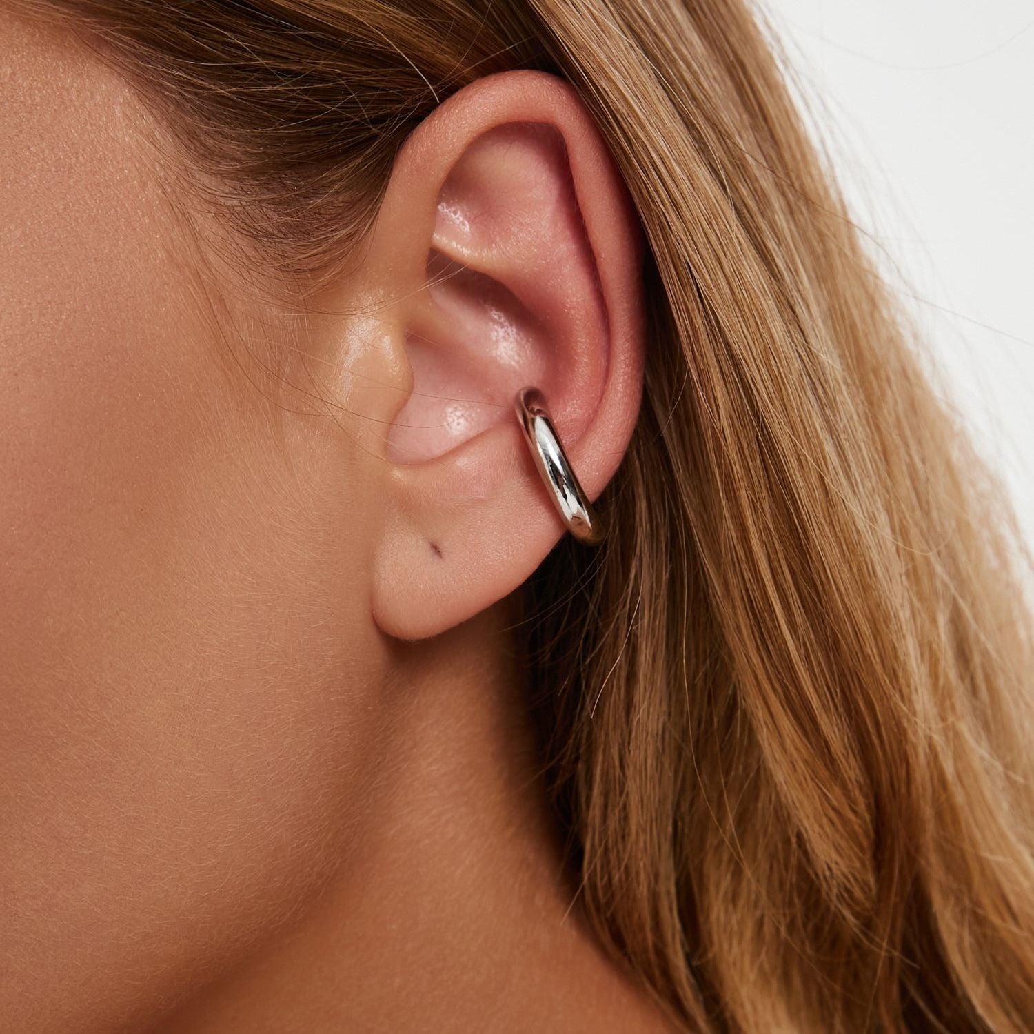 Earcuff Renude worn on an ear, showcasing its sleek gold-plated design and minimalist style.