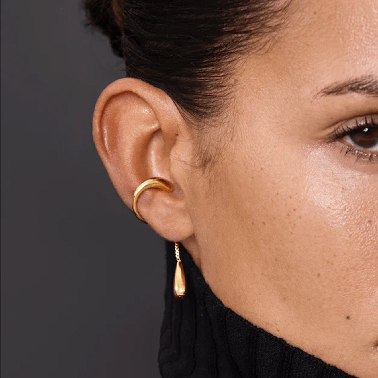 Earcuff Dew showcasing a gold-plated brass design with a smooth curve and a delicate droplet pendant.