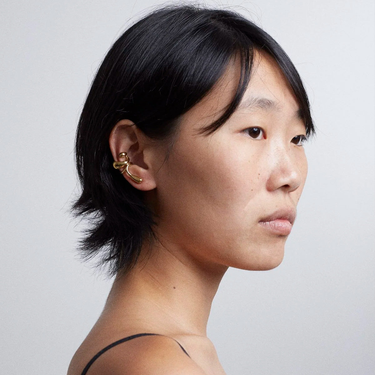 Model showcasing the Earcuff Lilt, a brass, gold-plated ear accessory with elegant curves.