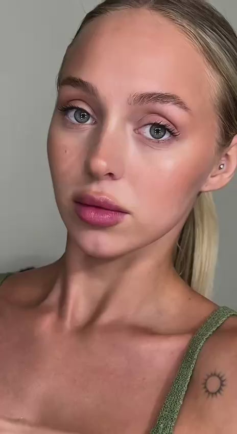 Close-up portrait of a young woman with green eyes and a natural makeup look, featuring a visible arm tattoo.