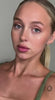 Close-up portrait of a young woman with green eyes and a natural makeup look, featuring a visible arm tattoo.
