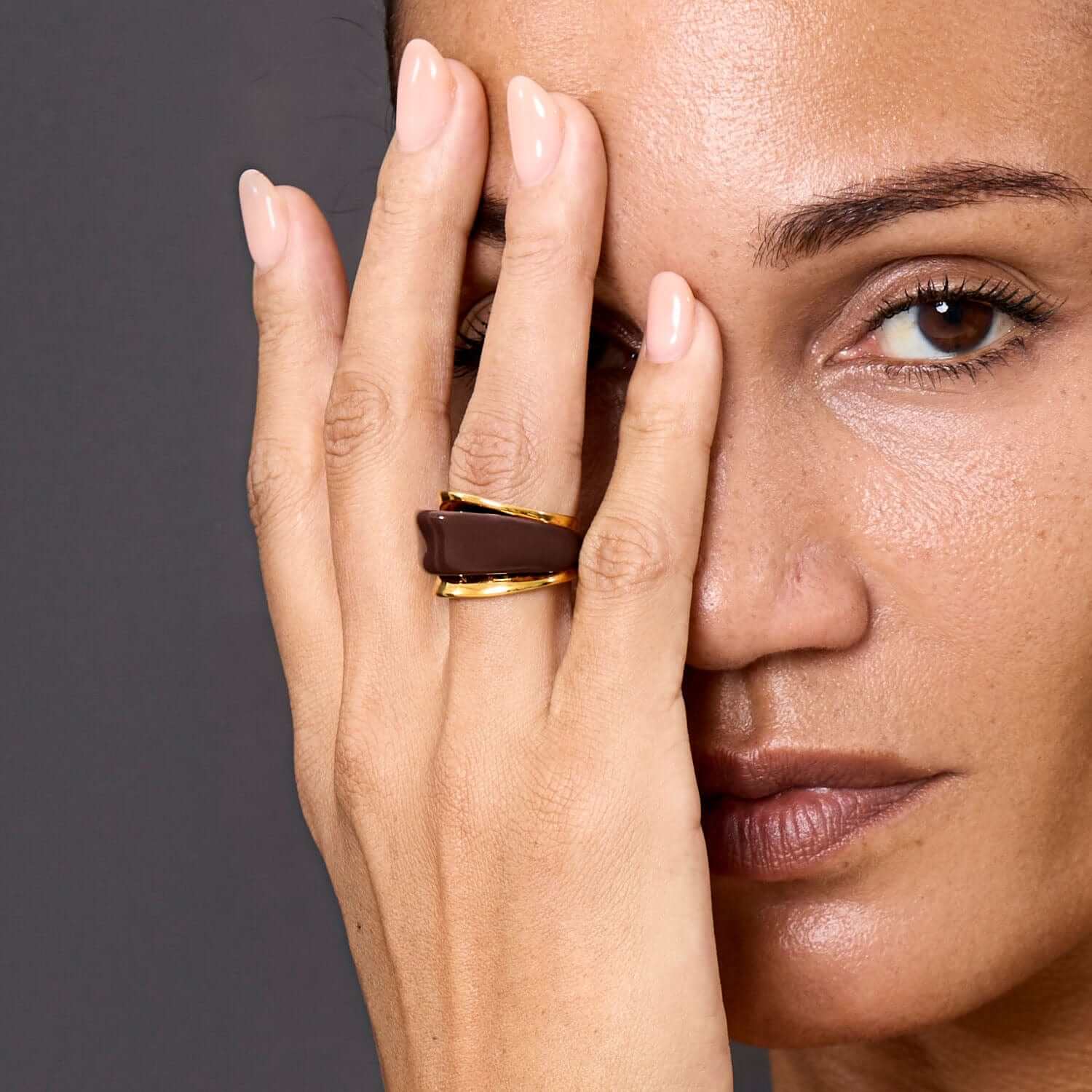 Model showcasing the Ring Terra, featuring gold-plated brass and warm brown enamel for elegant style.