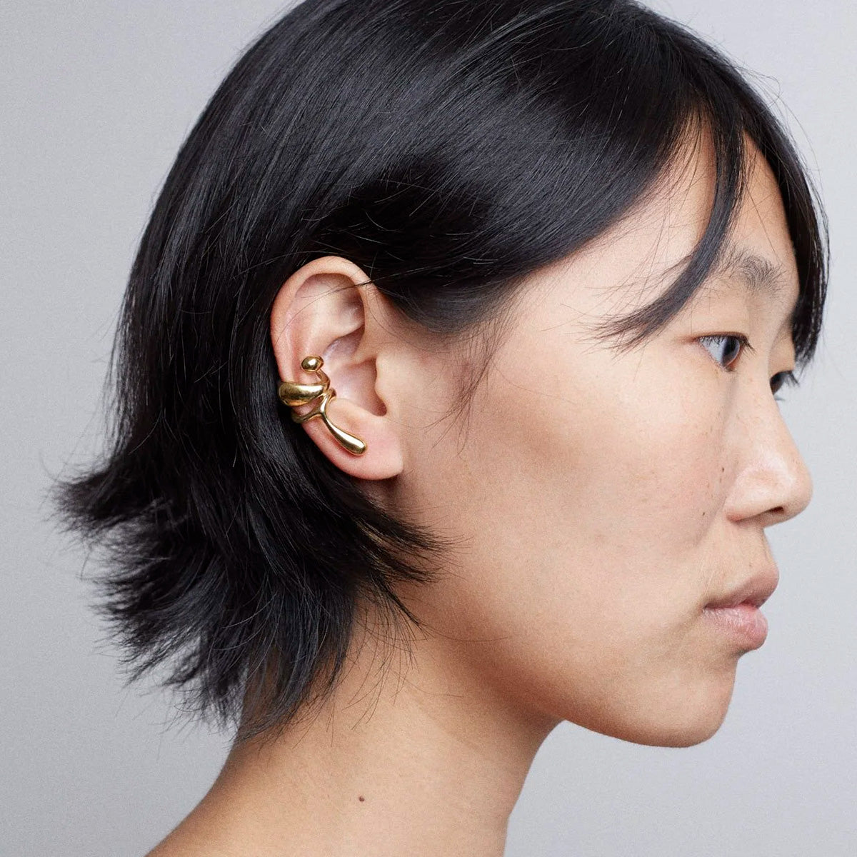 Earcuff Lilt worn by a model, showcasing its delicate gold-plated brass design and organic curves.